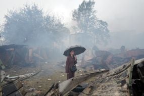 Жінка з парасолею оглядає знищені гаражі на одній з локацій після масованого удару по Києву