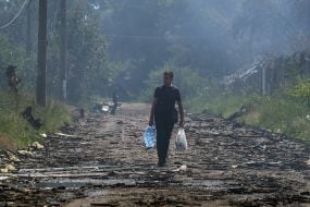 Чоловік несе пляшки з водою по задимленій внаслідок нічної російської атаки вулиці міста Вишневого