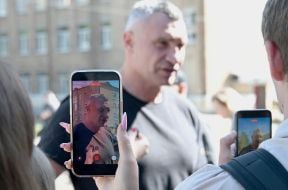 Віталій Кличко (на екрані мобільного телефону) відповідає на питання журналістів