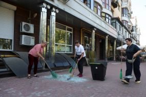 People clean up broken glass from windows after an enemy UAV crashed in the Obolonsky district of Kyiv