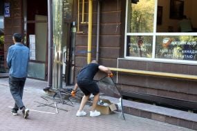 People clean up broken glass from windows after an enemy UAV crashed in the Obolonsky district of Kyiv