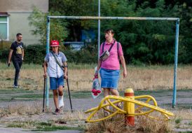 Мать сопровождает сына с травмой ноги в школу