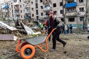 A volunteer near a damaged residential building.