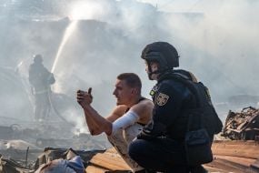 A psychologist from the State Emergency Service stands beside a man whose wife was killed in a strike by guided aerial bombs on a residential area of ​​Kharkiv