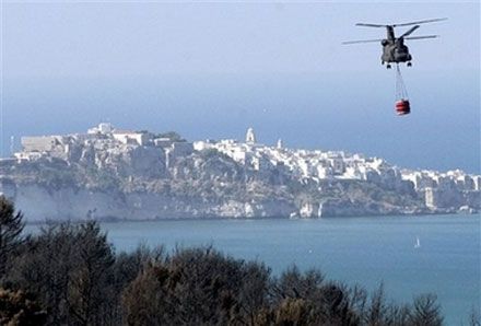 Вертолет итальянских ВМС, взяв в контейнер воду из Адриатического моря, направляется к месту пожара. (AP Photo)