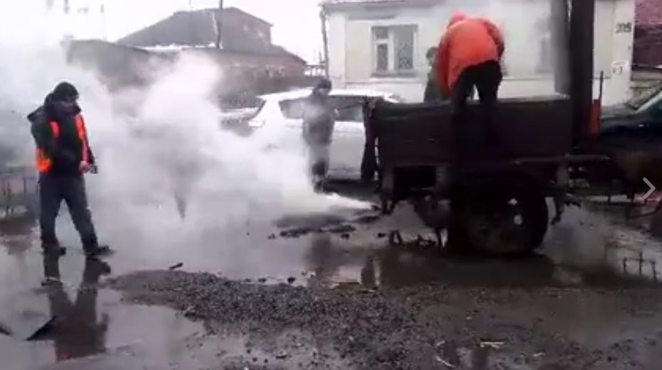 Чоловіки у спецодязі старанно засипають асфальт на ділянку дороги, залитий водою / Скріншот Чоловіки у спецодязі старанно засипають асфальт на ділянку дороги, залитий водою / Скріншот
