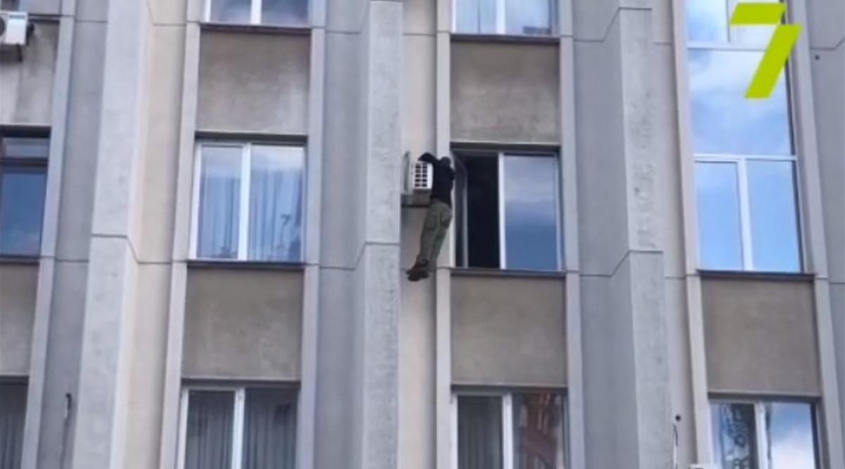 В итоге мужчина слез с подоконника в помещение / скриншот из видео В итоге мужчина слез с подоконника в помещение / скриншот из видео